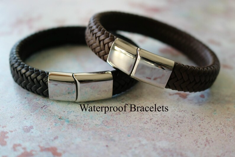 Op de afbeelding: Twee gevlochten lederen armbanden met zilveren magneetsluitingen. De armbanden zijn bruin en zwart. De tekst "Waterdichte armbanden" is zichtbaar onder de armbanden.