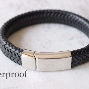 May include: A black leather bracelet with a braided design and a silver metal clasp. The bracelet is labeled "Waterproof".