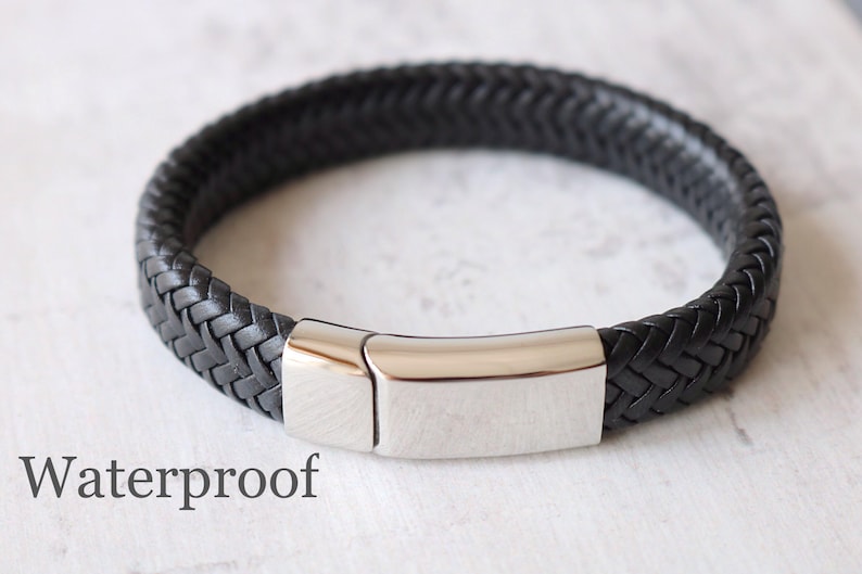 May include: A black leather bracelet with a braided design and a silver metal clasp. The bracelet is labeled "Waterproof".