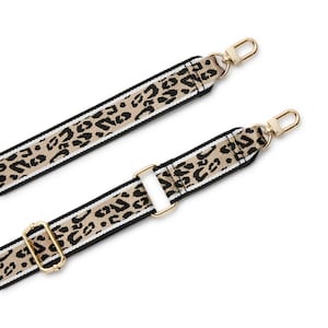 May include: A replacement bag strap featuring a tan and black leopard print pattern with white side stripes. The strap includes gold-toned metal hardware, including two swivel lobster clasps at the ends and two adjustable sliders for length modification.