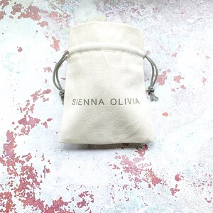 Op de afbeelding: Een witte trekkoordtas met de tekst "SIENNA OLIVIA" gedrukt op de voorkant.