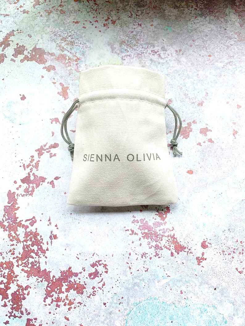 May include: A white drawstring pouch with the text "SIENNA OLIVIA" printed on the front.