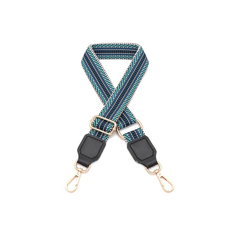 May include: A woven bag strap featuring a geometric pattern in navy blue, teal, and white. The strap includes a gold-toned metal adjustable slider and two gold-toned swivel lobster clasps attached to black faux leather tabs at each end.
