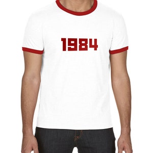 May include: White t-shirt with a red ringer and the number 1984 printed in red on the front.