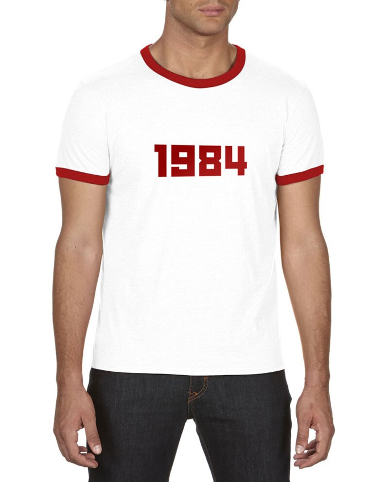 May include: White t-shirt with a red ringer and the number 1984 printed in red on the front.