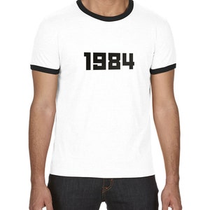 May include: White t-shirt with a black ringer and the number 1984 printed on the front.