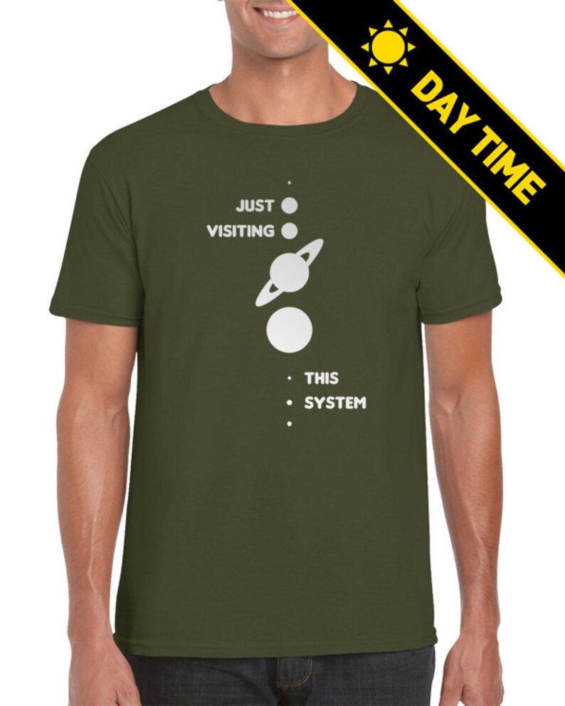 May include: A green t-shirt with white text that reads 'Just Visiting This System' and a graphic of a solar system with planets and a sun.