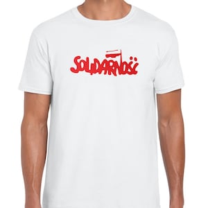 May include: White t-shirt featuring a red graphic of the word "Solidarność" in a stylised font with a small Polish flag above the word.