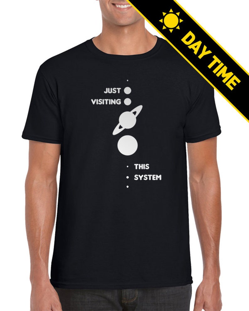 May include: A black t-shirt with a white graphic of a solar system with the text 'JUST VISITING THIS SYSTEM'.