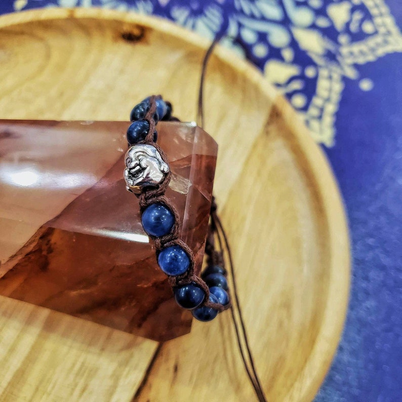 Peut inclure: Un bracelet en pierres bleues avec un charme argent&eacute; en forme de visage souriant. Le bracelet est fait de cordon marron et de perles bleues.