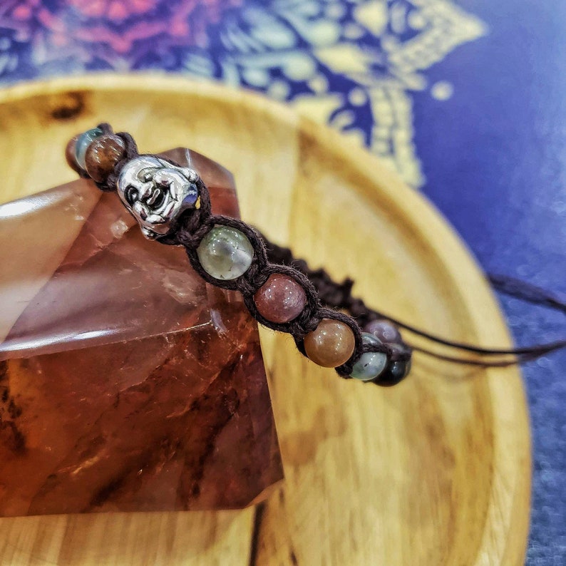 Peut inclure: Un bracelet en cuir marron avec des perles de pierres pr&eacute;cieuses multicolores et un charme en argent. Le bracelet est sur une surface en bois.