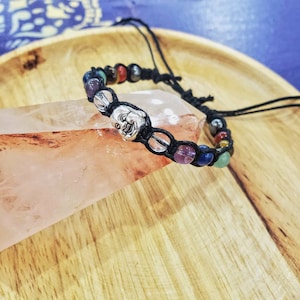 Peut inclure: Un bracelet en cordon noir avec des perles color&eacute;es et un charme en argent repr&eacute;sentant un visage de Bouddha souriant.