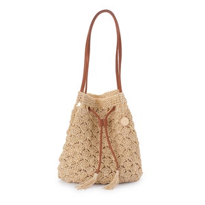 May include: A beige crochet bucket bag with brown leather handles and drawstring closure. The bag features a shell-like pattern and a small, round emblem. Tassels hang from the drawstring.
