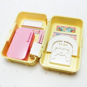 May include: A yellow plastic carrying case with a pink refrigerator, white chairs, and a white bed inside. The case is open and the items are visible.