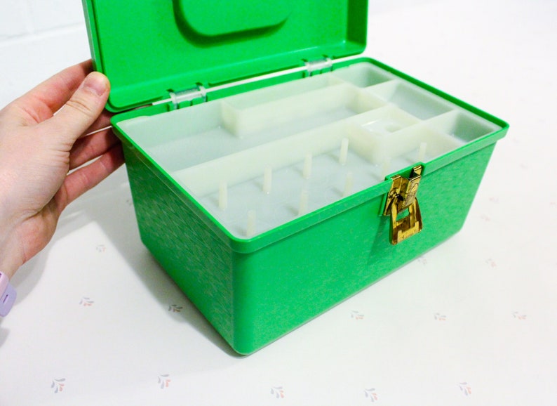 Puede incluir: Una caja de almacenamiento de pl&aacute;stico verde con un cierre y compartimentos en el interior. La caja est&aacute; abierta y la tapa est&aacute; levantada.