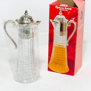 May include: A clear glass pitcher with a silver lid and handle. The pitcher is in its original box, which is red and has the words "Queen Anne" printed on it.