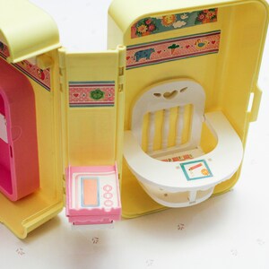 May include: A yellow plastic toy playhouse with a pink refrigerator, a white high chair, and a pink stove. The playhouse has a floral pattern on the outside.