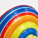 May include: A colorful spinning top with a red handle and a rainbow design. The top is made of metal and has a yellow center.
