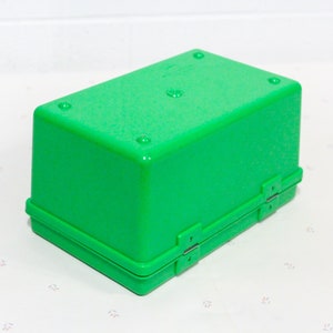 Puede incluir: Una caja de almacenamiento de pl&aacute;stico verde brillante con una tapa con bisagras y dos cierres. La caja est&aacute; cerrada y se encuentra sobre una superficie blanca.
