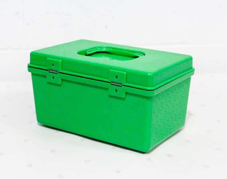 Puede incluir: Una caja de almacenamiento de pl&aacute;stico verde brillante con una tapa con bisagras y una manija de transporte. La caja tiene una superficie texturizada.