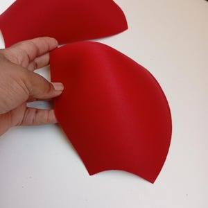 May include: Two molded bra cups in a vibrant red color. These foam inserts feature a smooth, rounded shape designed for garment construction. The cups are lightweight and flexible, showcasing a consistent solid red hue across the entire surface.