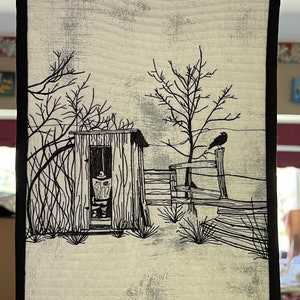 Peut inclure: Une tenture murale matelassée avec une scène rurale en noir et blanc. L'œuvre représente une petite cabane, une clôture et un corbeau perché sur un poteau. La scène est encadrée d'une bordure noire.