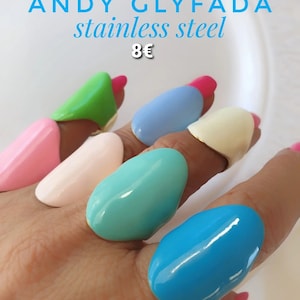 Puede incluir: Un conjunto de seis anillos coloridos hechos de acero inoxidable. Los anillos son de varios tonos de azul, verde, rosa y blanco. Los anillos son todos de forma ovalada y tienen un acabado brillante. El texto "ANDY GLYFADA stainless steel 8€" es visible en la parte superior de la imagen.