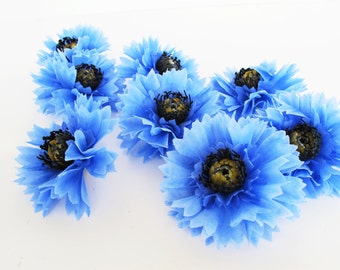 May include: A cluster of blue tissue paper flowers with black centers and yellow accents. The flowers are arranged on a white surface.