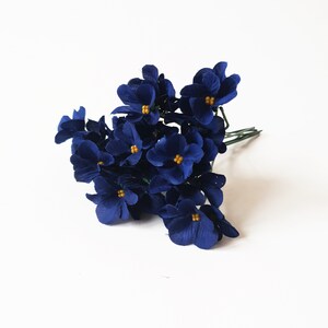 May include: A bunch of small, dark blue paper flowers with yellow centers. The flowers are arranged in a cluster and have a delicate, vintage look.