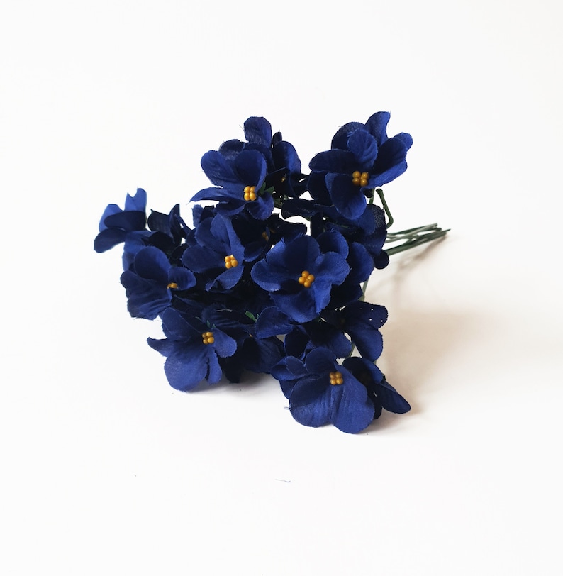 May include: A bunch of small, dark blue paper flowers with yellow centers. The flowers are arranged in a cluster and have a delicate, vintage look.
