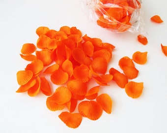Puede incluir: Una colección de pétalos de flores artificiales de color naranja vibrante esparcidos sobre una superficie, con una parte de los pétalos dentro de una bolsa de plástico transparente en la esquina superior derecha. Los pétalos tienen una superficie texturizada.