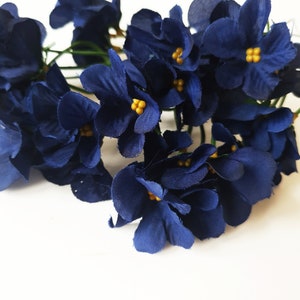 May include: A bunch of dark blue silk flowers with yellow centers. The flowers are arranged in a cluster and have a delicate, soft texture.