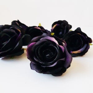 May include: A cluster of artificial rose heads in a deep black color with subtle hints of dark purple on the petal edges. Each flower features layered, rounded petals arranged in a classic bloom shape, with small green sepals visible at the base.
