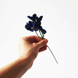 May include: A bunch of small blue fabric flowers with yellow centers on a green wire stem.