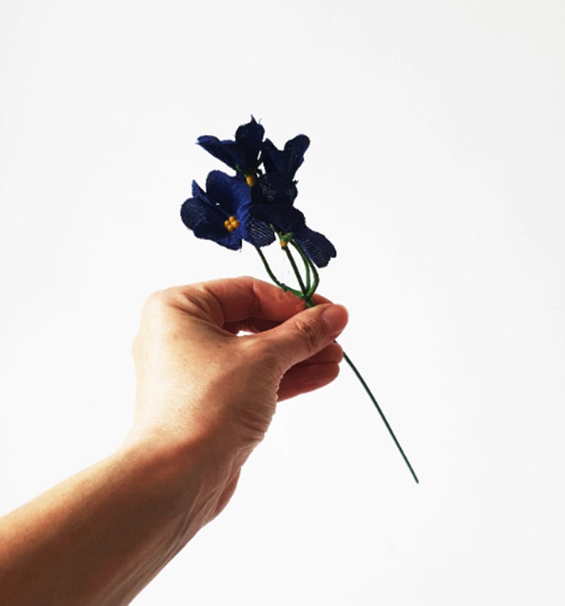 May include: A bunch of small blue fabric flowers with yellow centers on a green wire stem.