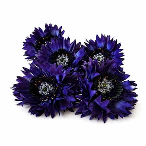 Puede incluir: Un grupo de cuatro flores artificiales con pétalos de color azul real intenso. Cada flor presenta un centro negro oscuro rodeado de pequeños detalles translúcidos en forma de cuentas que imitan la apariencia de granos de polen en el estambre.