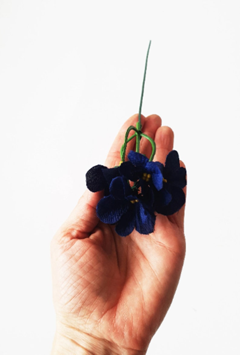 May include: A bunch of small, dark blue velvet flowers with yellow centers. The flowers are attached to a green stem.