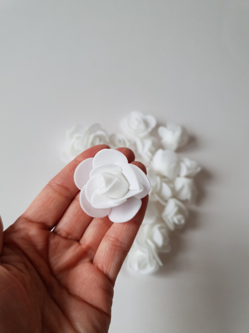 K&ouml;nnte beinhalten: Eine Sammlung kleiner, wei&szlig;er k&uuml;nstlicher Rosenbl&uuml;ten aus Schaumstoff. Jede Bl&uuml;te besteht aus geschichteten, abgerundeten Bl&uuml;tenbl&auml;ttern, die in einer klassischen Rosenform angeordnet sind. Die Bl&uuml;ten haben eine matte Textur und eine einheitliche Farbe.
