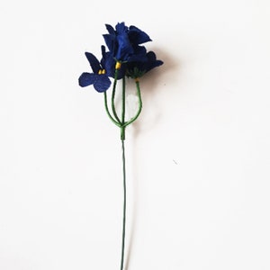 May include: A single stem of artificial blue flowers with yellow centers. The flowers are made of fabric and are attached to a green wire stem.