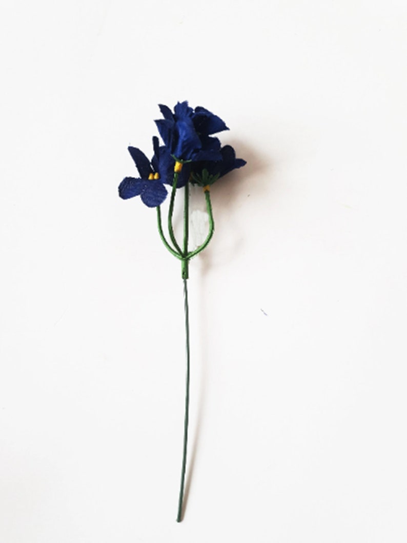 May include: A single stem of artificial blue flowers with yellow centers. The flowers are made of fabric and are attached to a green wire stem.