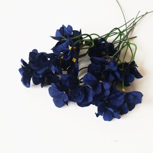 May include: A bunch of dark blue silk flowers with yellow centers. The flowers are arranged in a bouquet and have green stems.