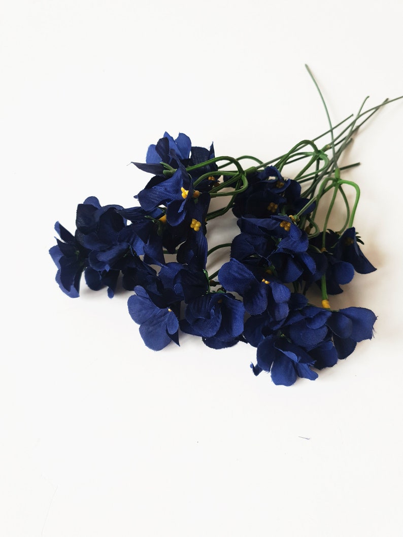 May include: A bunch of dark blue silk flowers with yellow centers. The flowers are arranged in a bouquet and have green stems.