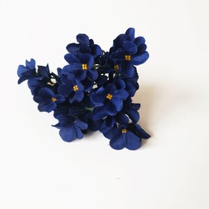 May include: A cluster of small, dark blue artificial flowers with yellow centers. The flowers are arranged in a bunch and have a velvety texture.