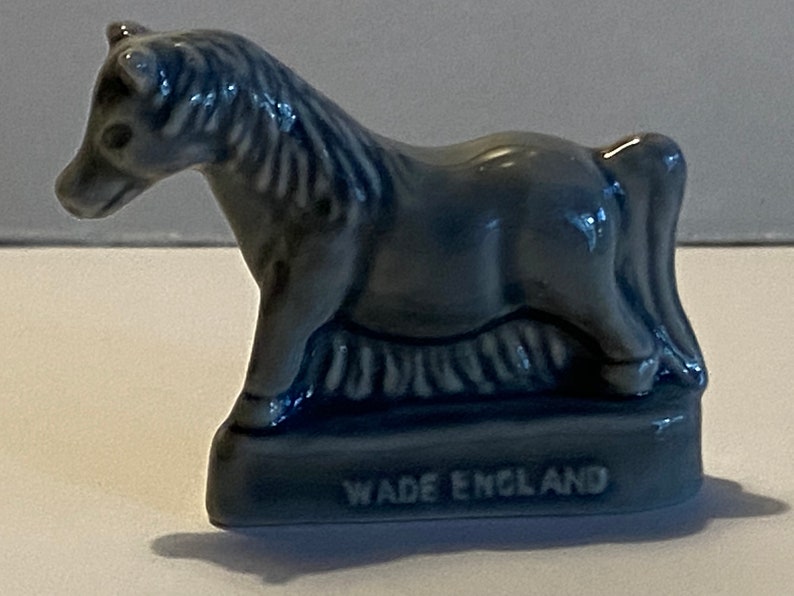 Pu&ograve; includere: Una piccola figurina di ceramica blu di un cavallo, in piedi su una base con le parole "Wade England" incise su di essa.