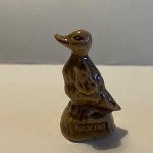 Pu&ograve; includere: Una statuetta di ceramica marrone di un'anatra in piedi su una piccola base. La base ha le parole "Wade Eng" stampate.