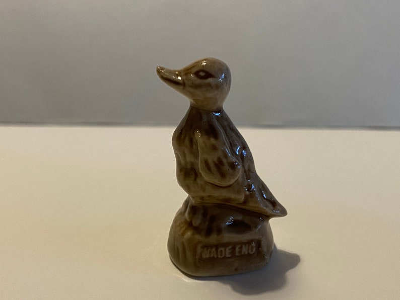 Pu&ograve; includere: Una statuetta di ceramica marrone di un'anatra in piedi su una piccola base. La base ha le parole "Wade Eng" stampate.