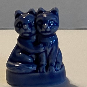 Pu&ograve; includere: Una statuetta in ceramica blu di due gatti che si abbracciano. I gatti sono seduti su una base e hanno i volti bianchi.