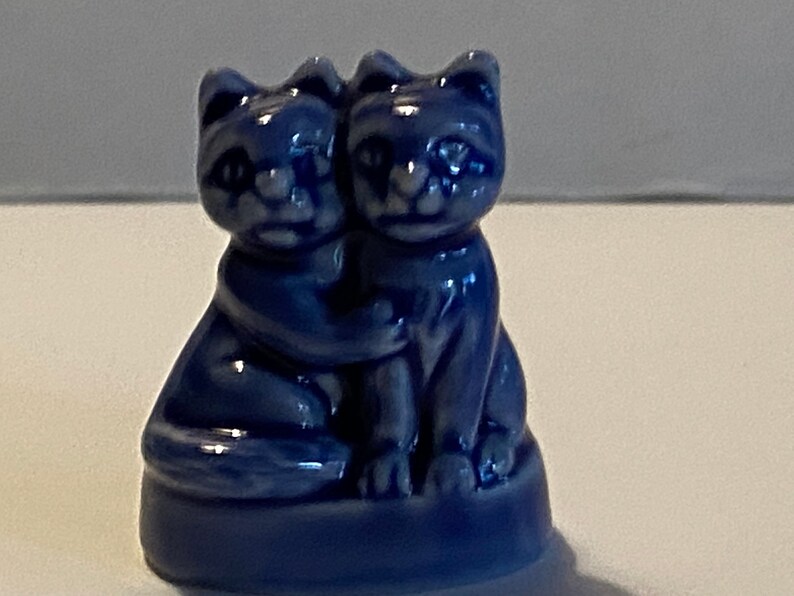 Pu&ograve; includere: Una statuetta in ceramica blu di due gatti che si abbracciano. I gatti sono seduti su una base e hanno i volti bianchi.