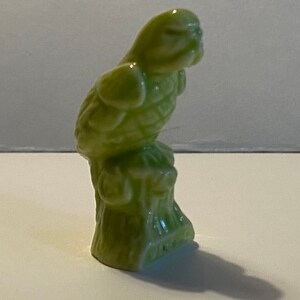 Pu&ograve; includere: Una statuetta di ceramica verde di un pappagallo appollaiato su un ceppo d'albero. Il pappagallo &egrave; rivolto a sinistra e ha la testa inclinata verso il basso.