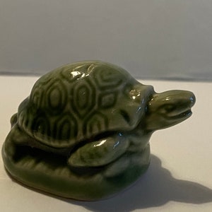 Pu&ograve; includere: Una statuetta di tartaruga in ceramica verde con un motivo a guscio dettagliato. La tartaruga &egrave; seduta su una base e ha la testa girata di lato.